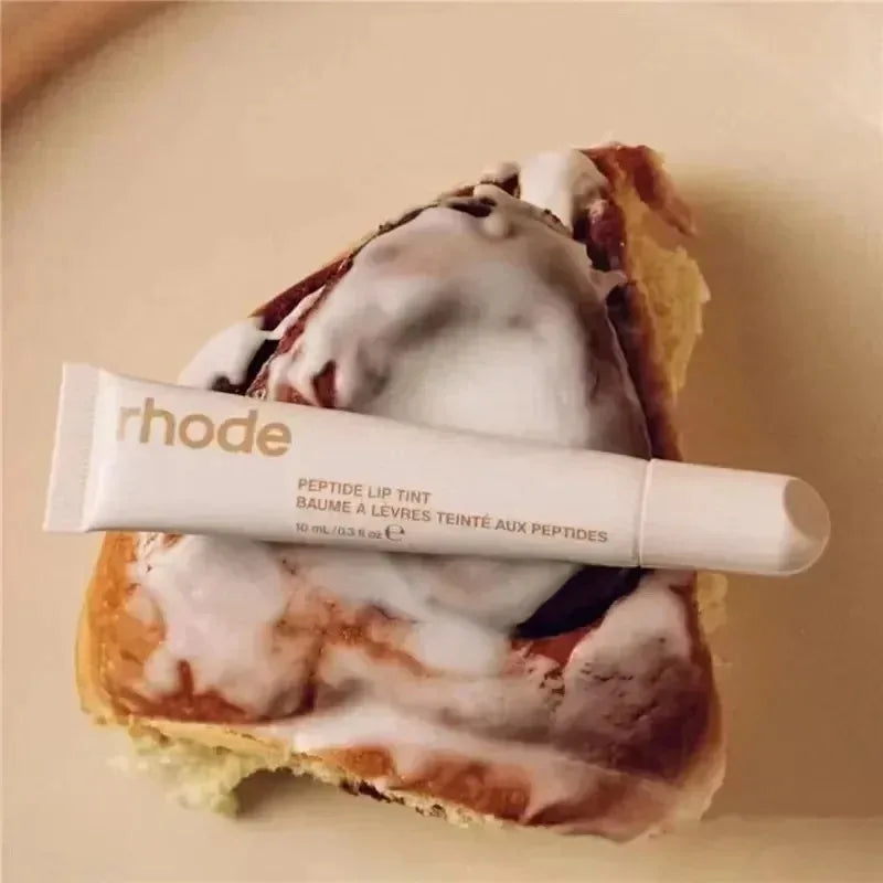 Tube of 'rhode' lip tint on a piece of cake with white frosting