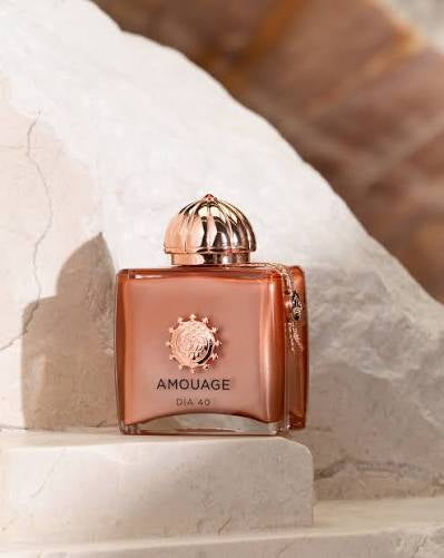 Amouage Dia 40 perfume bottle in a metallic copper-rose color with a matching dome cap, displayed on a white stone pedestal.