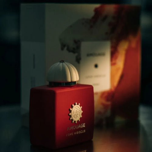 Amouage Love Hibiscus perfume bottle in a deep red glass with a cream-colored ribbed cap, set against its branded packaging box.