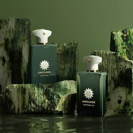 Two Amouage Purpose 50 perfume bottles in dark green with white caps, styled on mossy rocks against a matching green background.
