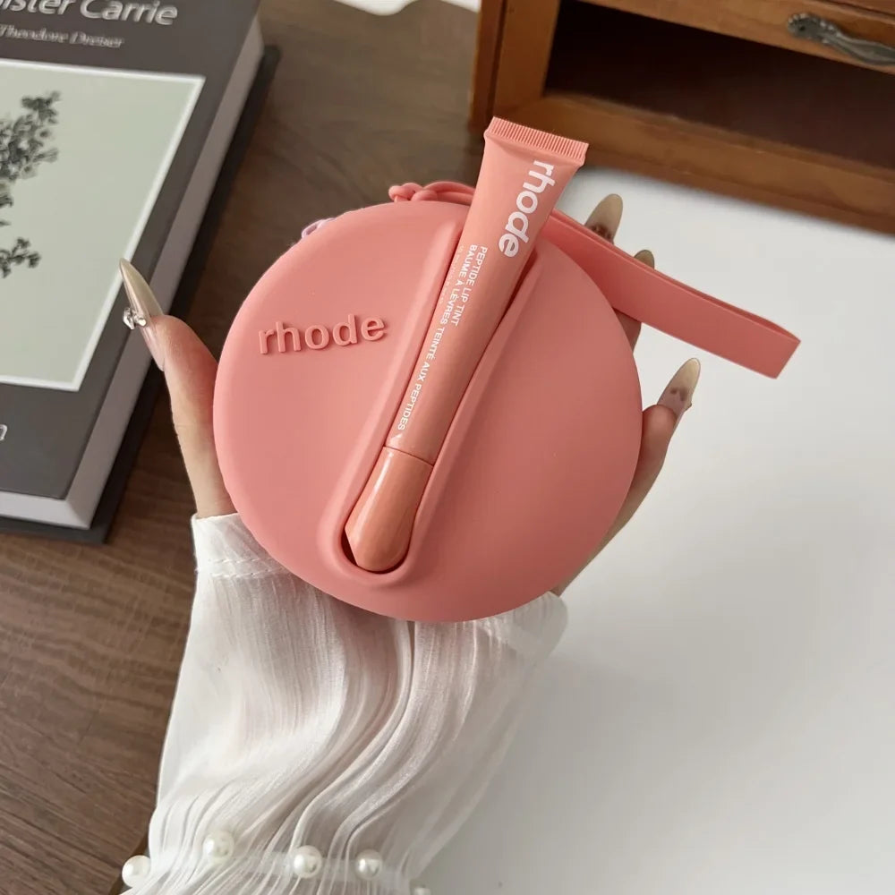 Pink lip balm case with 'rhode' branding held by a hand on a wooden surface.