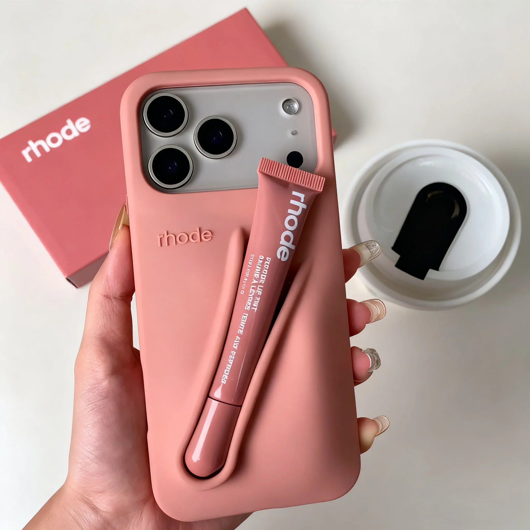 Pink phone case with matching lipstick held by a hand, with 'rhode' branding.